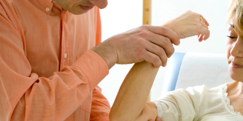 Wanneer moet je testen op reuma_ Foto van een dokter die de bewegelijkheid van de arm van zijn client test. Om uit te beelden hoe een reuma test werkt en wanneer je moet testen op reuma